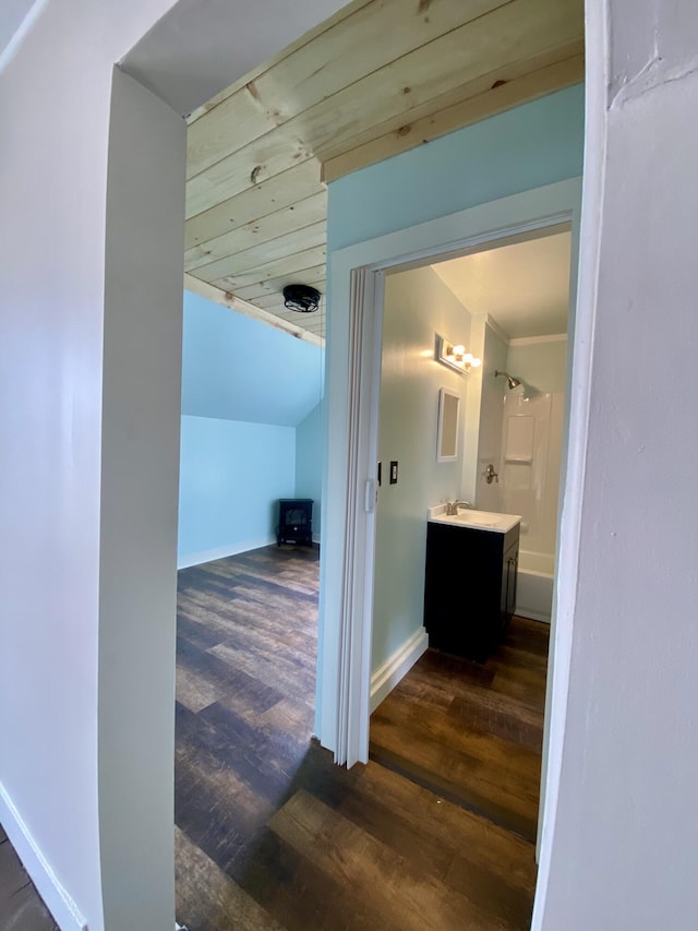 corridor with dark wood finished floors, a sink, baseboards, and vaulted ceiling
