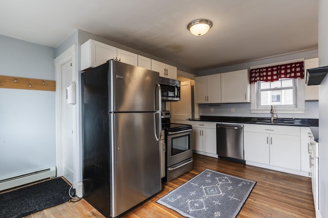 kitchen featuring a baseboard heating unit, dark wood finished floors, appliances with stainless steel finishes, white cabinets, and a sink