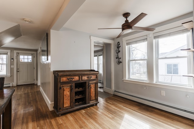 foyer entrance with a baseboard radiator, a healthy amount of sunlight, a ceiling fan, and hardwood / wood-style flooring