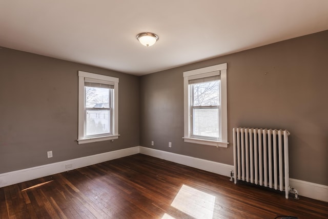 spare room with dark wood-type flooring, radiator heating unit, baseboards, and a wealth of natural light