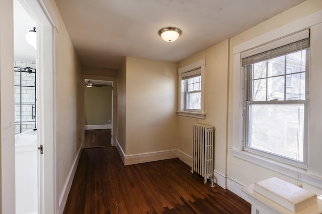 hall with dark wood-type flooring, radiator heating unit, and baseboards