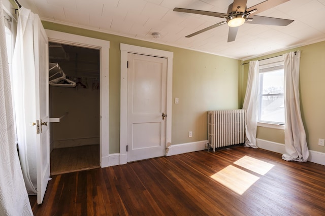 unfurnished bedroom featuring a walk in closet, baseboards, wood finished floors, and radiator heating unit