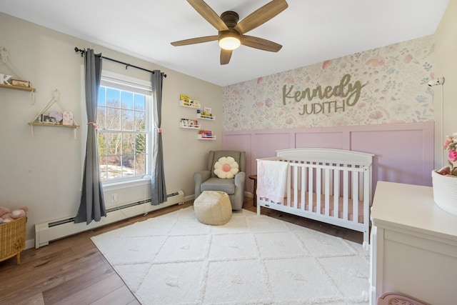 63 Grandview Dr, Newport, ME 04953 - bedroom featuring a baseboard heating unit, wainscoting, wallpapered walls, wood finished floors, and a nursery area