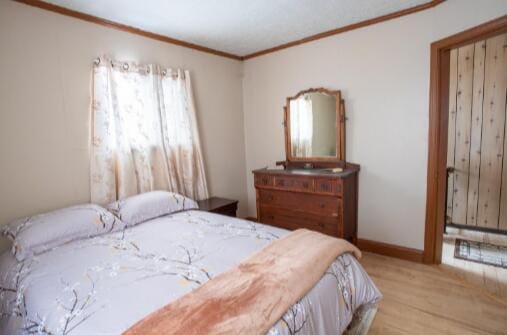 bedroom with baseboards, wood finished floors, and crown molding