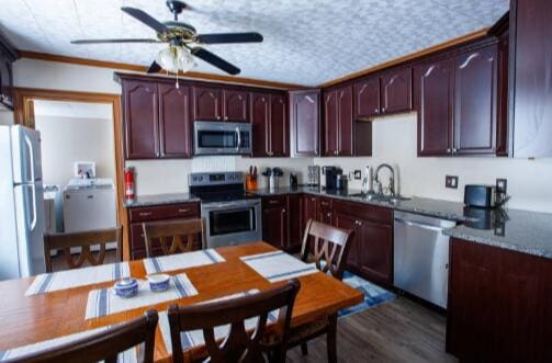 kitchen featuring dark countertops, stainless steel appliances, a textured ceiling, a ceiling fan, and a sink