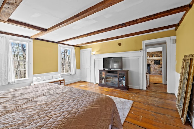 30 Joy Valley Rd, Buxton, ME 04093 - bedroom featuring a brick fireplace, beamed ceiling, hardwood / wood-style flooring, and a wainscoted wall