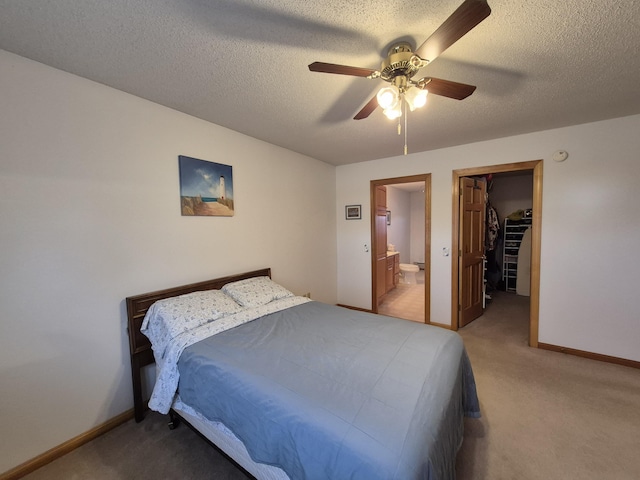 bedroom with light carpet, a spacious closet, ensuite bathroom, and baseboards