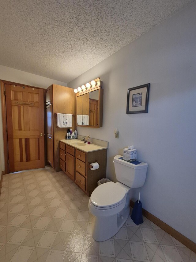 bathroom featuring a textured ceiling, toilet, vanity, and baseboards