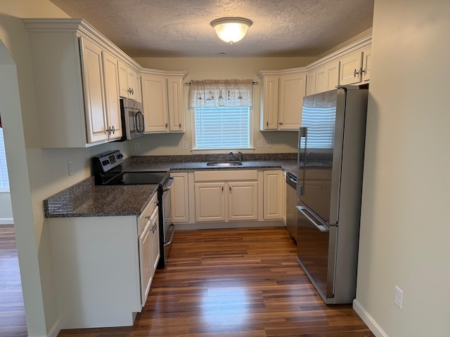 kitchen with a sink, a textured ceiling, appliances with stainless steel finishes, white cabinets, and dark wood-style flooring