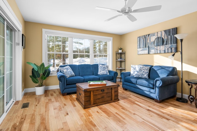 living room with visible vents, light wood-style flooring, a ceiling fan, and baseboards