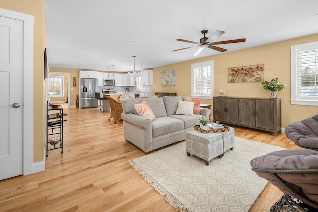 living room featuring a healthy amount of sunlight, baseboards, light wood-style flooring, and a ceiling fan