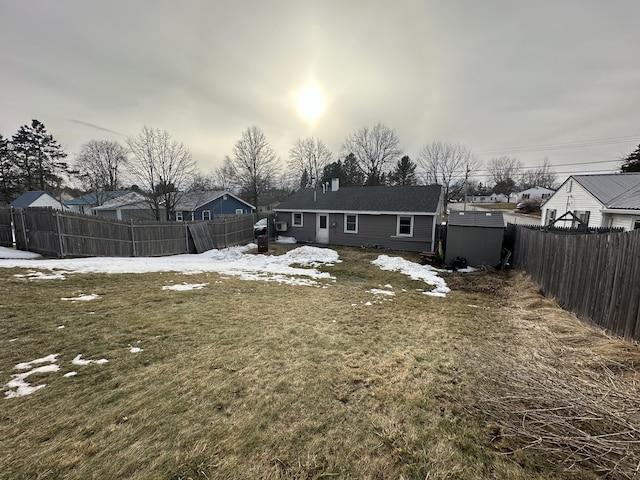 snow covered rear of property with a lawn, a fenced backyard, a residential view, a storage shed, and an outdoor structure
