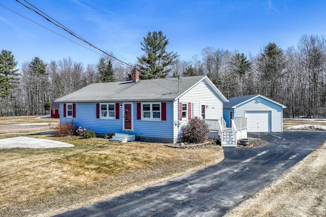 single story home featuring a detached garage, aphalt driveway, a front yard, a chimney, and an outbuilding