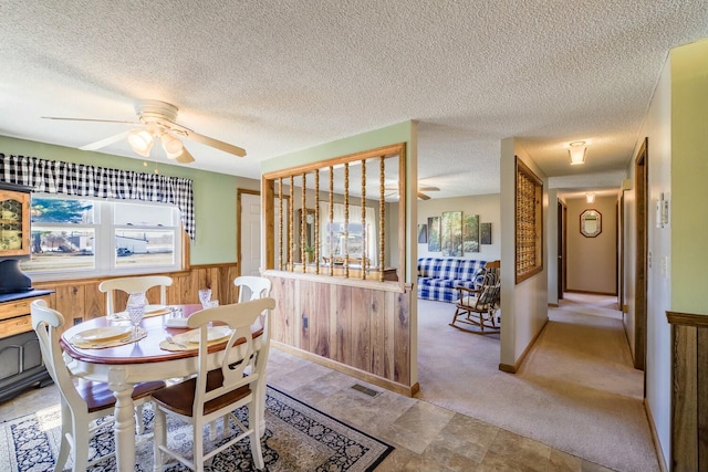 dining room with a ceiling fan, visible vents, a wainscoted wall, wood walls, and a textured ceiling