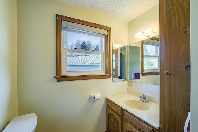 half bath with vanity, toilet, and a textured ceiling