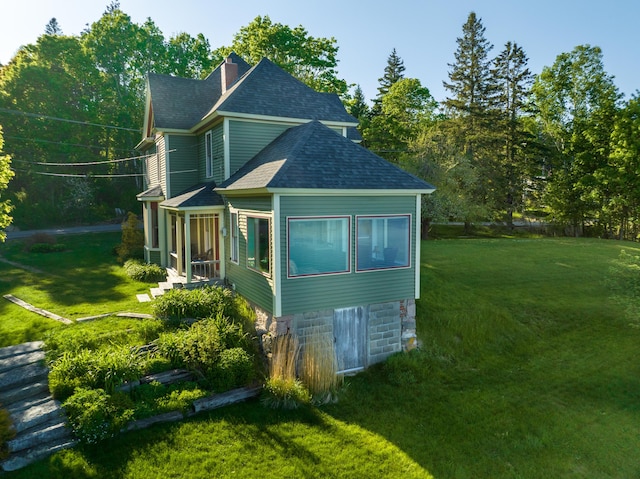 view of side of home with a lawn, roof with shingles, and a chimney