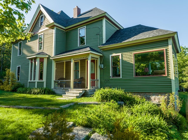 rear view of property with a porch, a lawn, a shingled roof, and a chimney