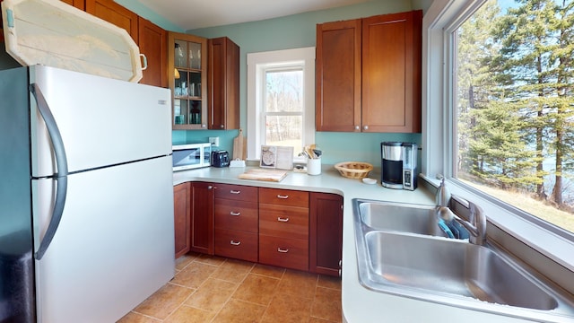 kitchen with a sink, freestanding refrigerator, white microwave, glass insert cabinets, and light countertops