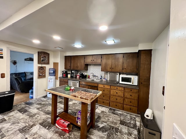 kitchen featuring dark countertops, tasteful backsplash, stainless steel dishwasher, a sink, and white microwave
