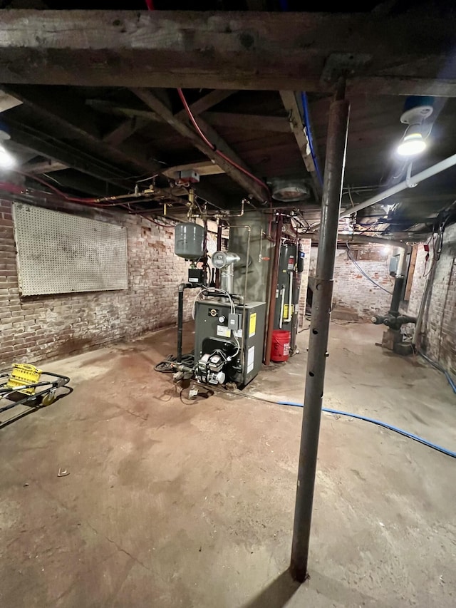 unfinished below grade area with a heating unit, water heater, and brick wall