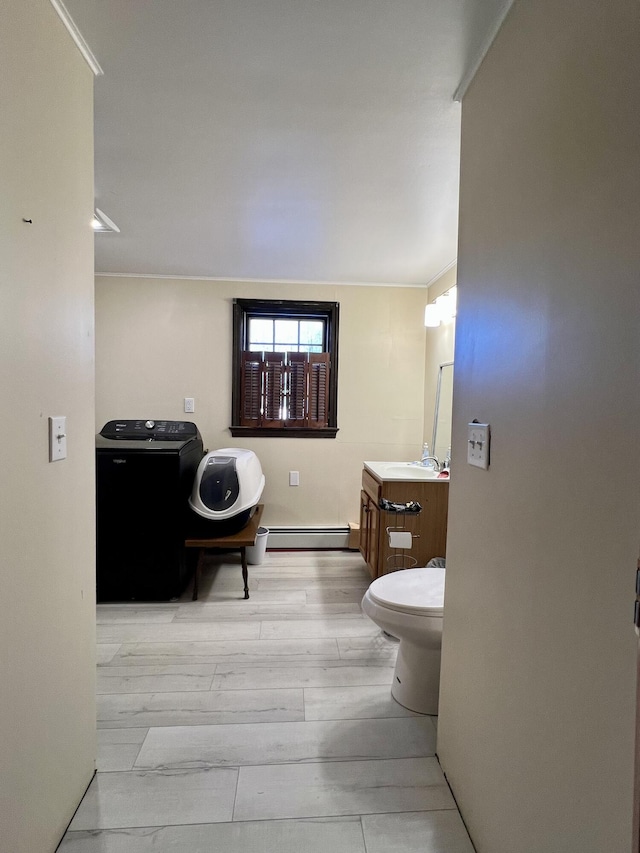 bathroom featuring baseboard heating, wood finished floors, vanity, toilet, and washer / dryer