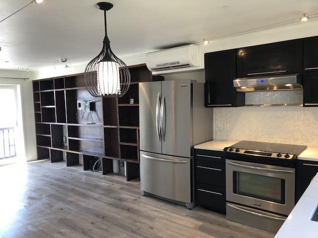 kitchen with dark cabinetry, range hood, light wood-style flooring, an AC wall unit, and appliances with stainless steel finishes