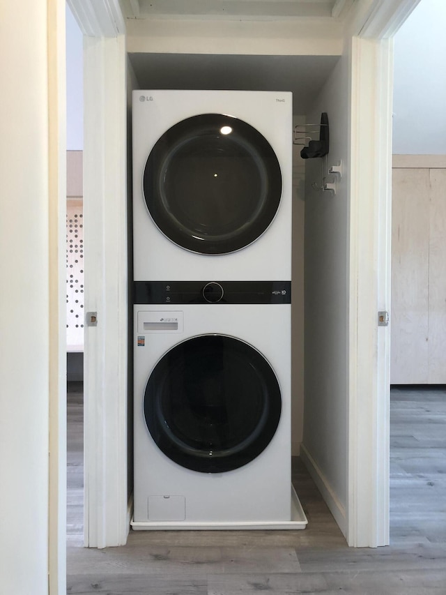 clothes washing area with laundry area, stacked washer and clothes dryer, and wood finished floors