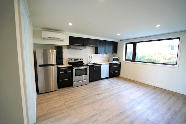 kitchen featuring a wall mounted air conditioner, under cabinet range hood, a sink, backsplash, and stainless steel appliances