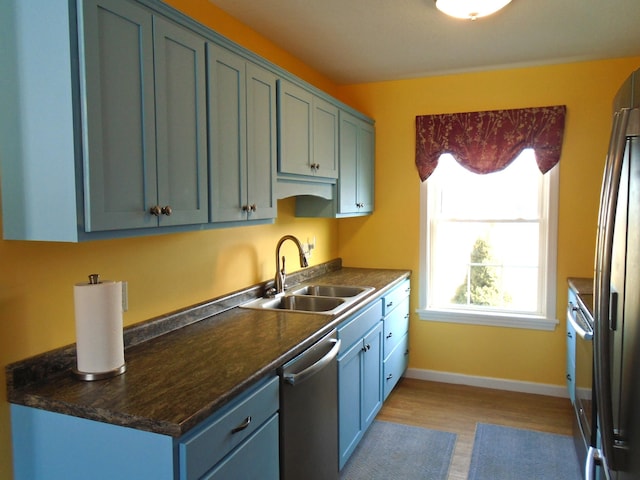 kitchen featuring dark countertops, baseboards, appliances with stainless steel finishes, light wood-style floors, and a sink