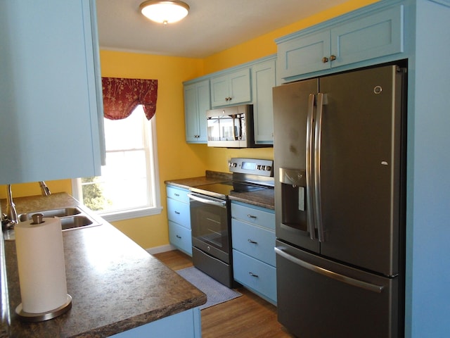 kitchen featuring a sink, blue cabinetry, appliances with stainless steel finishes, and dark wood-style floors