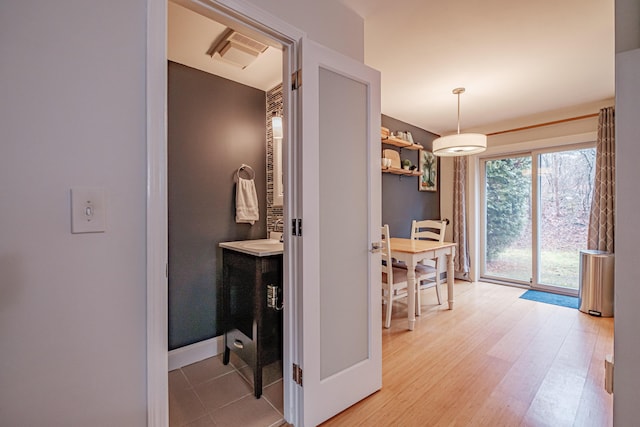 hall with visible vents, baseboards, light wood-style floors, and a sink