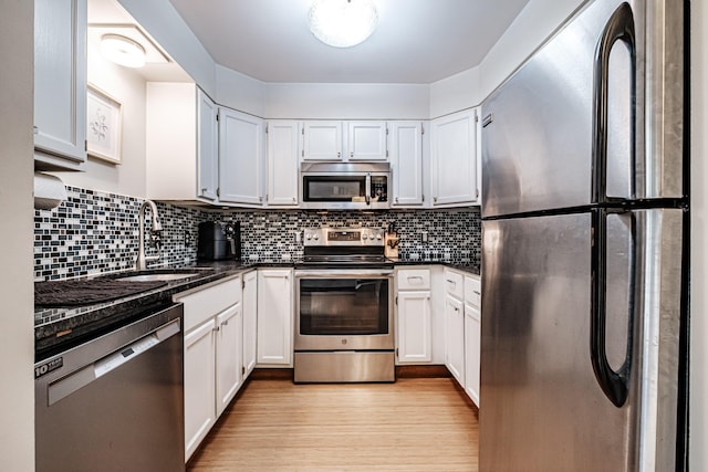 kitchen with a sink, light wood-type flooring, dark countertops, and appliances with stainless steel finishes