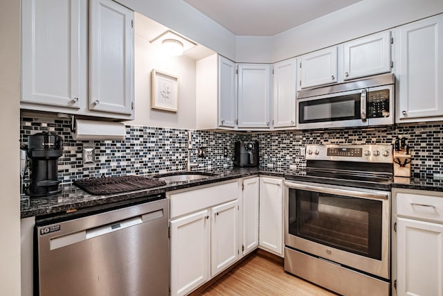 kitchen featuring tasteful backsplash, dark stone countertops, stainless steel appliances, and light wood-style floors