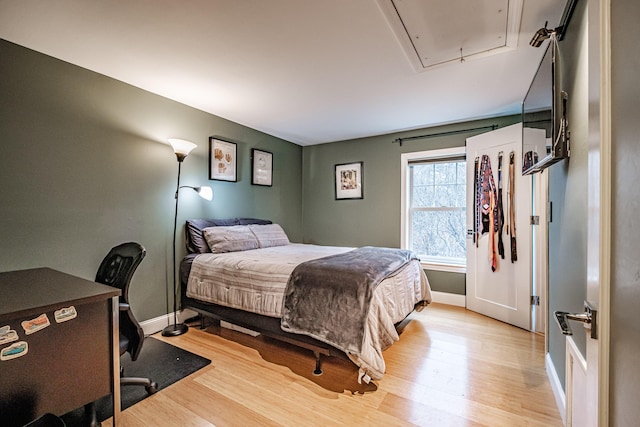 bedroom with baseboards, attic access, and light wood finished floors