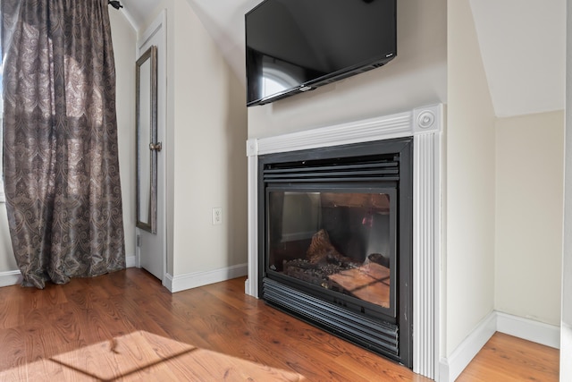 details with a glass covered fireplace, baseboards, and wood finished floors