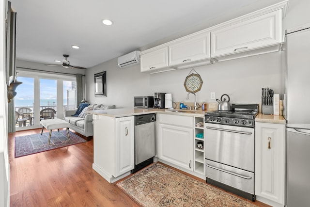 kitchen featuring an AC wall unit, a ceiling fan, a sink, stainless steel appliances, and white cabinets