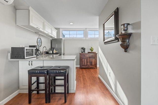 kitchen with a kitchen breakfast bar, appliances with stainless steel finishes, white cabinets, light wood finished floors, and baseboards