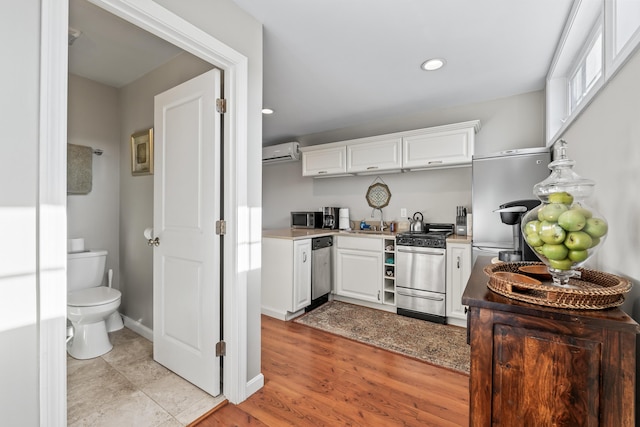 kitchen with a sink, white cabinetry, a wall unit AC, stainless steel appliances, and baseboards