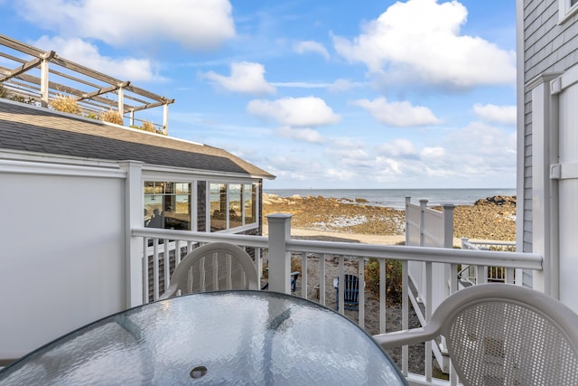 balcony featuring a beach view, outdoor dining area, and a water view