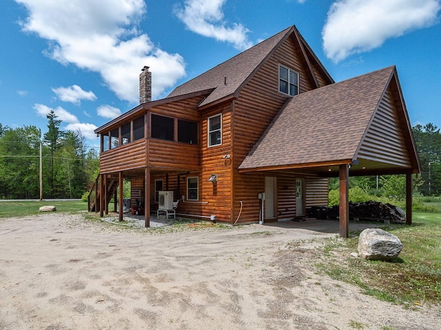 back of house with roof with shingles, a chimney, a sunroom, driveway, and log veneer siding