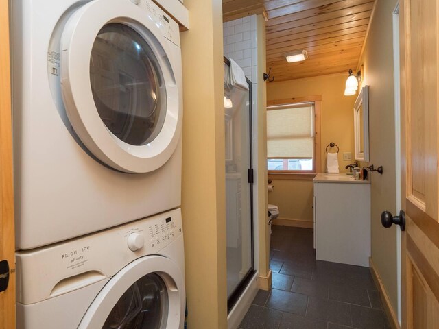 laundry room featuring baseboards, laundry area, stacked washer and clothes dryer, wooden ceiling, and a sink