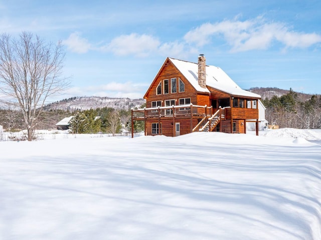 snow covered rear of property featuring stairway, faux log siding, a deck with mountain view, and a chimney