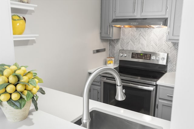 kitchen with gray cabinetry, open shelves, backsplash, stainless steel range with electric cooktop, and wall chimney exhaust hood