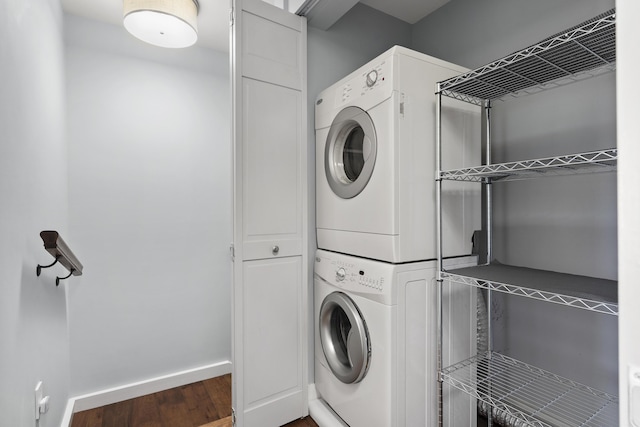 clothes washing area with baseboards, stacked washer and dryer, wood finished floors, and laundry area