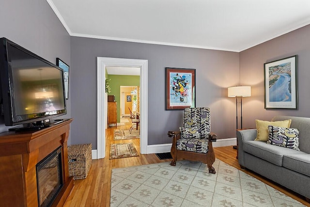 living area with a glass covered fireplace, baseboards, ornamental molding, and light wood finished floors