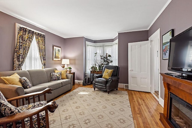 living area with a glass covered fireplace, baseboards, light wood-style flooring, and ornamental molding