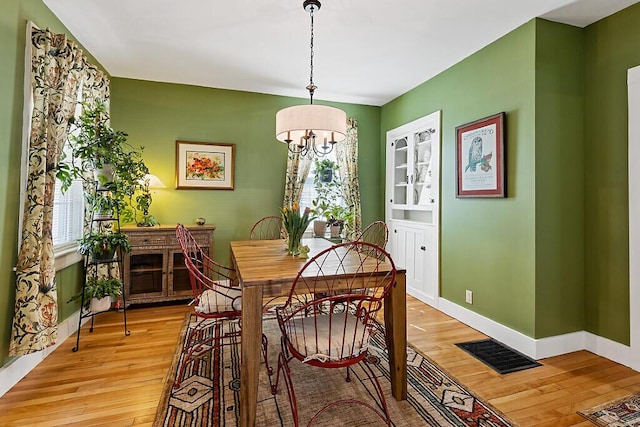 dining room with an inviting chandelier, light wood-style flooring, baseboards, and visible vents