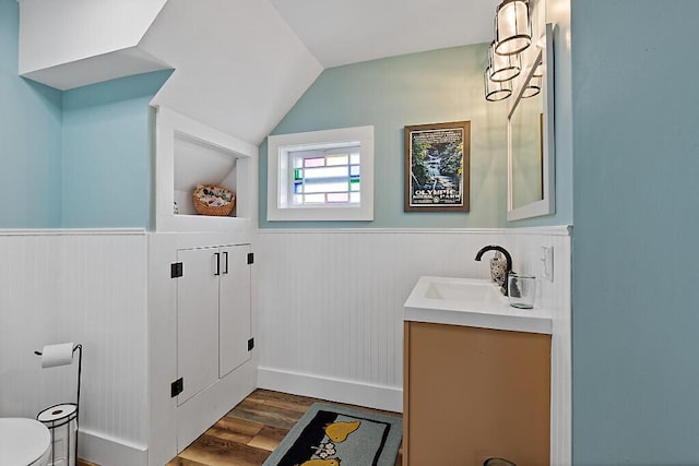half bathroom featuring toilet, wood finished floors, wainscoting, vanity, and vaulted ceiling