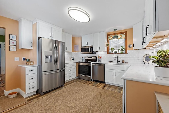 kitchen featuring a sink, backsplash, wood finished floors, stainless steel appliances, and white cabinets