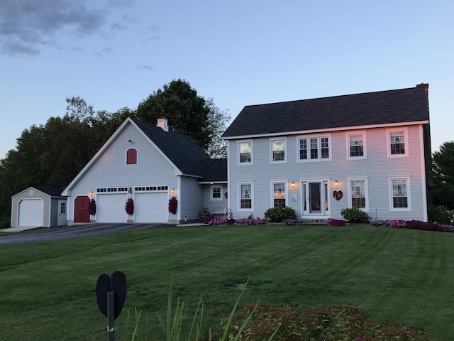 colonial home featuring a front yard, a garage, driveway, and a chimney